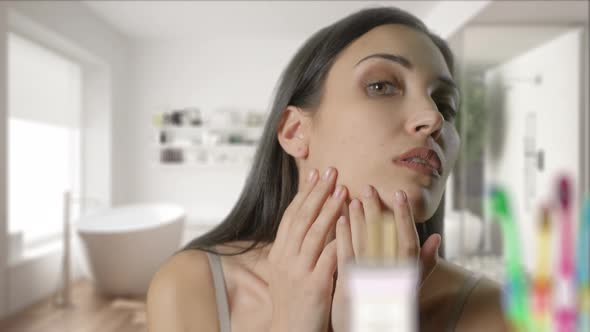 Young Woman Is Checking Her Face in Bathroom Mirror at Home. The Pretty Girl Is Looking To Mirror alt