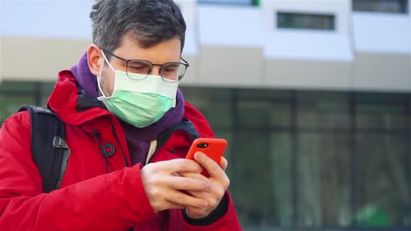 Man in Sterile Protective Mask Using His Phone on Street and Looking To Camera alt