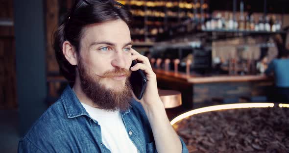 Bearded Man Talking on Smartphone in Cafe