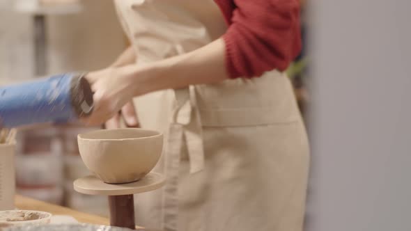 Female Potter Drying Clay Bowl with Heat Gun and Checking Surface alt