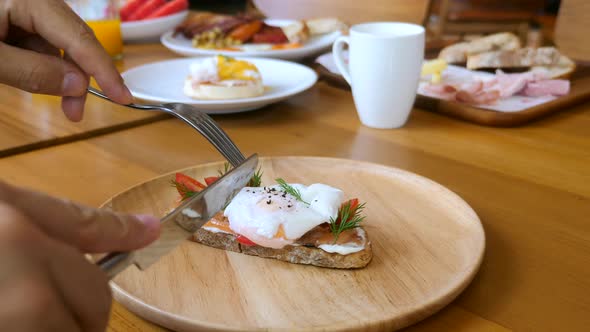 Male Hands with Fork and Knife Cut Egg Benedict with Liquid Yolk on Toast alt