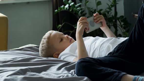 Portrait of A Child Boy Looking at the Phone Screen Playing a Game on a Smartphone alt