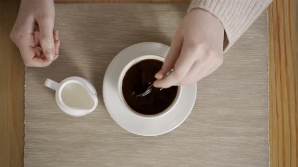 A Woman's Hand Is Stirring Americano and a Creamer Is Standing Nearby alt
