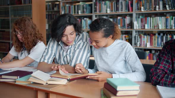 Cheerful Students Talking Reading Books in Library Making Project Together alt