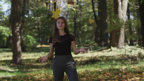 Girl Is Covering Her Face and Waving a Maple Tree Branch with Yellow Leaves in Autumn Park. Slow alt