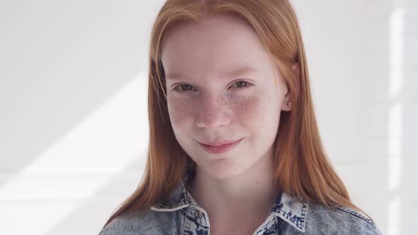 Happy Ginger Teenage Girl with Freckles Smiling Against White Wall