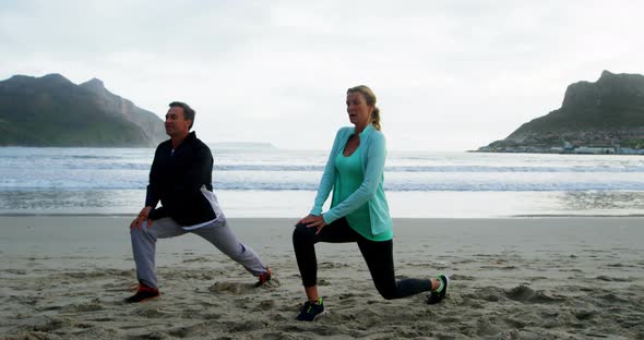 Mature couple performing stretching exercise on beach alt