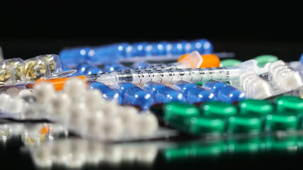Some Different Contraceptive Pills and Two Syringes, Rotation, Reflection, Close Up, on Black alt