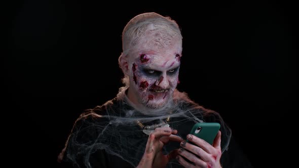 Frightening Man Halloween Zombie Using Mobile Phone Typing New Post on Web Browsing Addiction alt