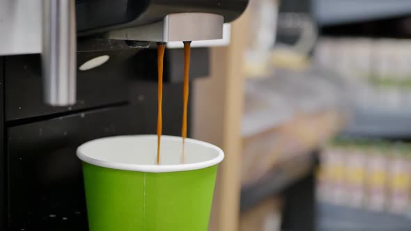 Two Jets of Cappuccino are Poured Into a Green Paper Cup in a Coffee Maker