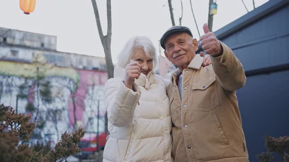 Stylish Elderly Couple Gives Thumbs Up to the Camera Standing on a Sunny Street