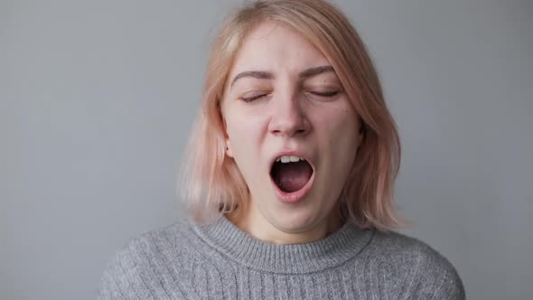 Portrait of a Young Tired Woman Looking at the Camera and Yawning