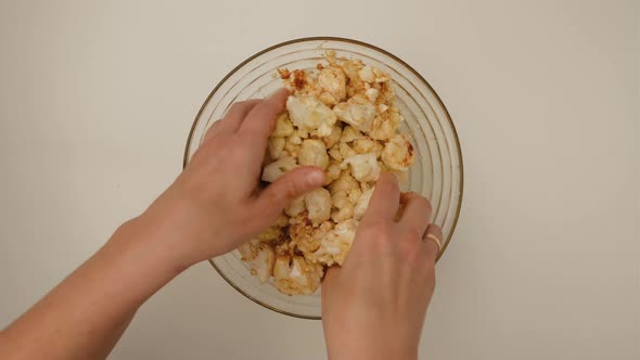 Top view of woman hands mixes cauliflower with paprika and olive oil in bowl alt