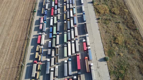 The drone flies over a long line of trucks standing in the port terminal waiting to be unloaded. alt