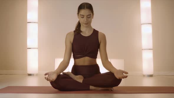 Woman Sitting in Lotus Pose on Mat Indoors. Trainer Practicing Yoga in Studio alt