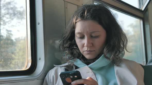 Focused Woman Rides a Train with a Phone in Her Hands and Carefully Reads the Messages on the Screen alt
