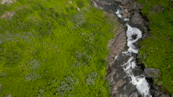 Aerial flyover idyllic Norwegian stream along green mountains in Norway alt