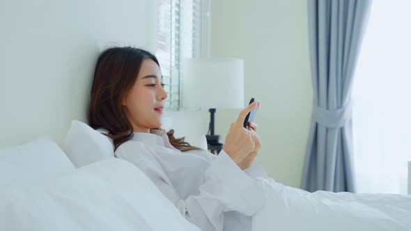 Asian attractive woman use mobile phone chat on bed at home in morning lying down and enjoy holiday. alt