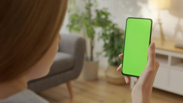 Back View of Woman at Living Room Using Phone With Green Mockup Screen Chroma Key Without Track alt