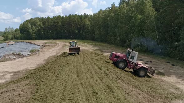 Drone view of tractors tamp the silage in the Silo Trench next to the forest 10 alt
