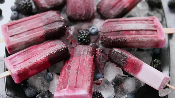 Homemade Fresh Frozen Blueberry and Blackberry Popsicles on Black Plate with Ice Sitting on Stone alt