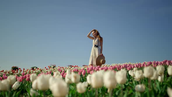 Camera Tracking Around Young Woman with Camera Enjoying Sunny Day in Tulip Field alt