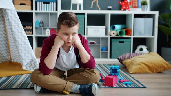 Slow Motion of Lonely Child Sitting on Floor in Playroom Feeling Miserable and Bored alt