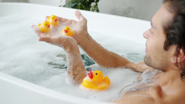 Slow Motion of Playful Adult Man Having Fun with Rubber Toys in Bathtub at Home alt