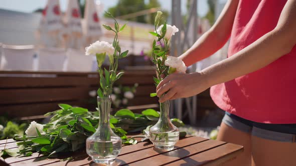 Caucasian Female with Brown Hair and Pink Shirt Puttinf Dlowers Into Vases with Water Outdoors alt