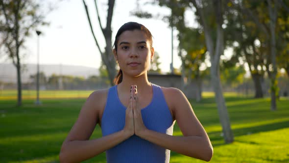 A pretty woman in a prayer hands yoga pose meditating in the park at sunrise. alt