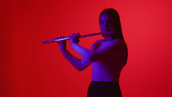 Smooth flute playing on colored background. Girl in a white blouse plays wind instrument flute alt
