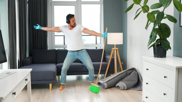 Man in Headphones Cleaning the House and Having Fun Dancing with a Broom alt