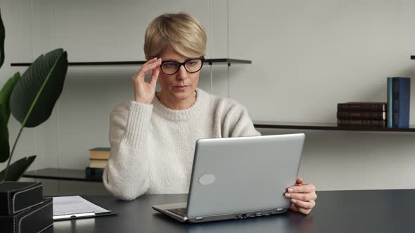 A Middleaged Business Woman Sitting at Her Desk Takes Off Her Glasses From the Pain in Her Eyes and alt