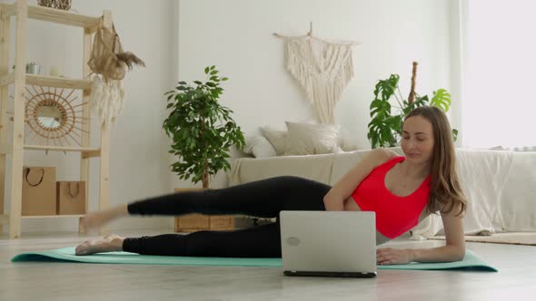 Leg Raise From Lying Position of a Young Woman She is Doing Her Exercises at Home Using a Laptop alt