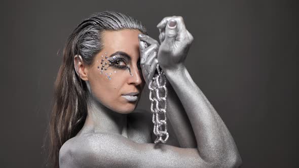 Beautiful Woman with Silver Paint on Her Skin and Hair Plays with a Chain in Her Hands