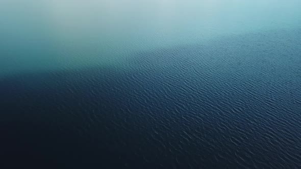 Birds eye view of a lake with different shades of blue and light waves from the wind above the water alt