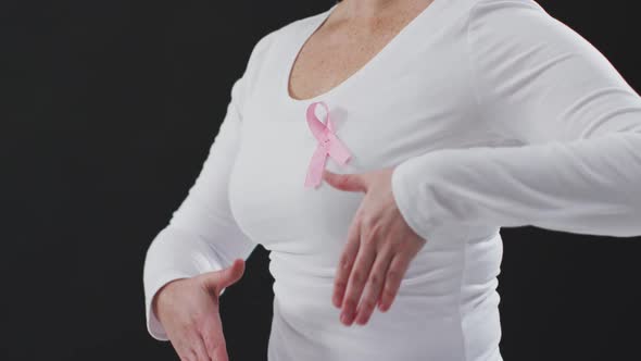 Mid section of a woman showing the pink ribbon on her chest against black background alt