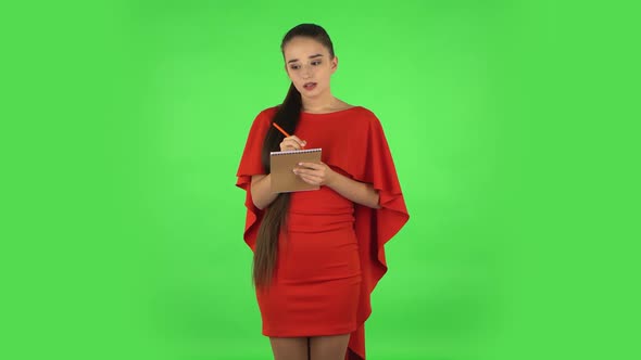 Pretty Young Woman Is Standing and Thinking, Then Happy Writing with Pencil in Notebook. Green alt