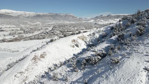 Aerial flight along a frozen hillside toward the town of Eagle with fresh snow during December. Film alt