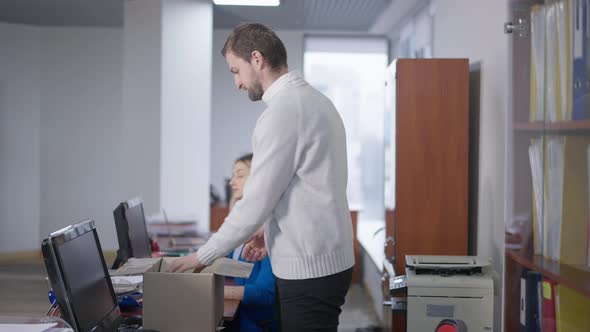 Brunette Bearded Caucasian Man Packing Belongings in Office in Cardboard Box alt