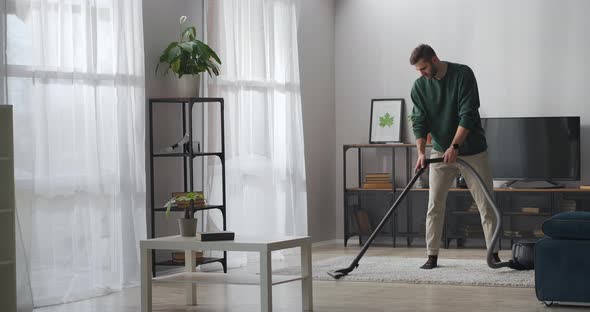 Adult Handsome Man Is Hoovering Carpet in Apartment Using Vacuum Cleaner for Cleaning Room at alt