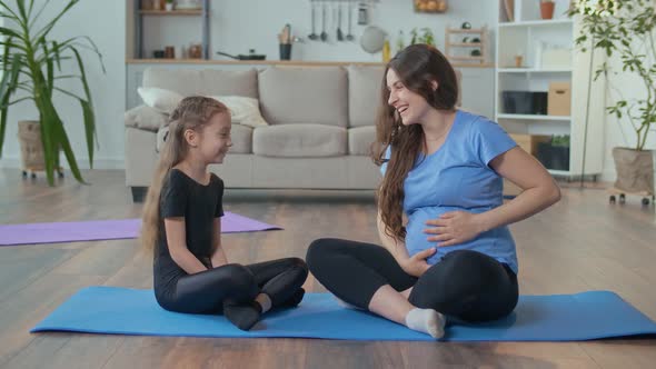 Pregnant Woman with a Child Doing Fitness at Home Mom is Talking to Her Daughter alt