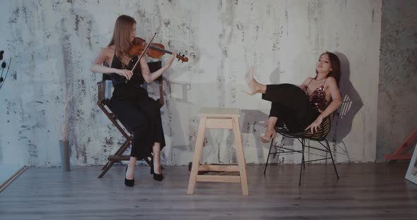 Lady Throws Her Legs on the Table and Having Fun While Girl Playing the Violin alt