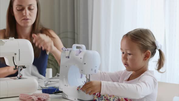 A Girl Is Sewing on a Machine. Mom Shows How To Work with Equipment. Close-up.