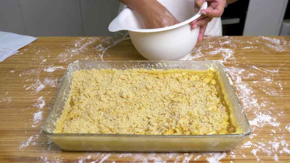 Female adding crumble on top of sliced apple for crumble pie cooking alt