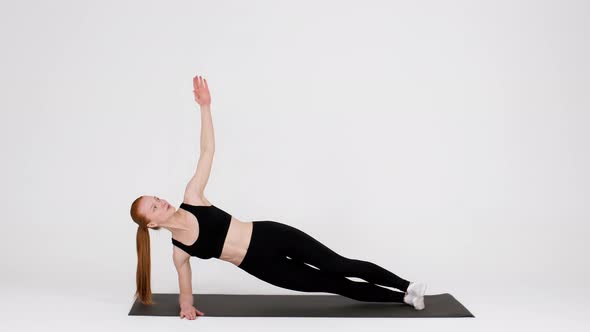 Athletic Young Woman Doing Side Plank Rotations Exercise While Training In Studio alt