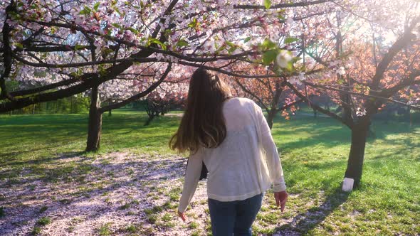 Young woman with long hair enjoys spring garden in bloom. Girl walking in Japanese Garden alt