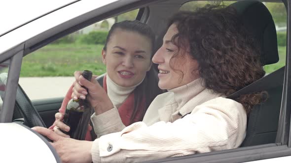 Two Girlfriends Drink Wine From a Bottle While Sitting in the Car