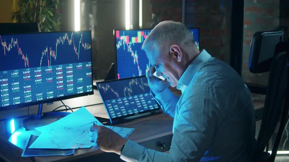 Male Trader is Talking on the Phone While Observing Stock Reports alt