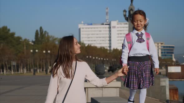 School Girl Is Walking on Railing of Seafront with Mom, Steadicam, Front View. alt